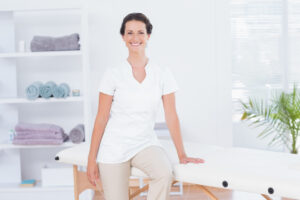 Medical massage therapist is wearing white and sitting on a table